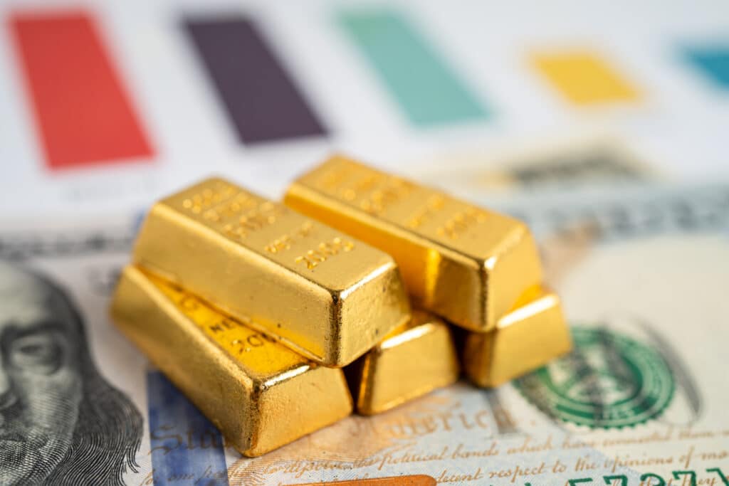 Goldbarren auf Dollarnoten und Diagrammen liegend.